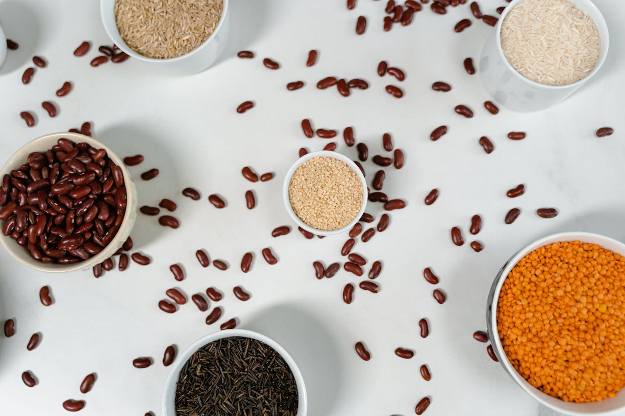 Top view of various grains and pulses in bowls on a white surface.